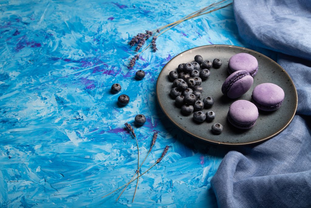 Purple macarons or macaroons cakes with blueberries on ceramic p