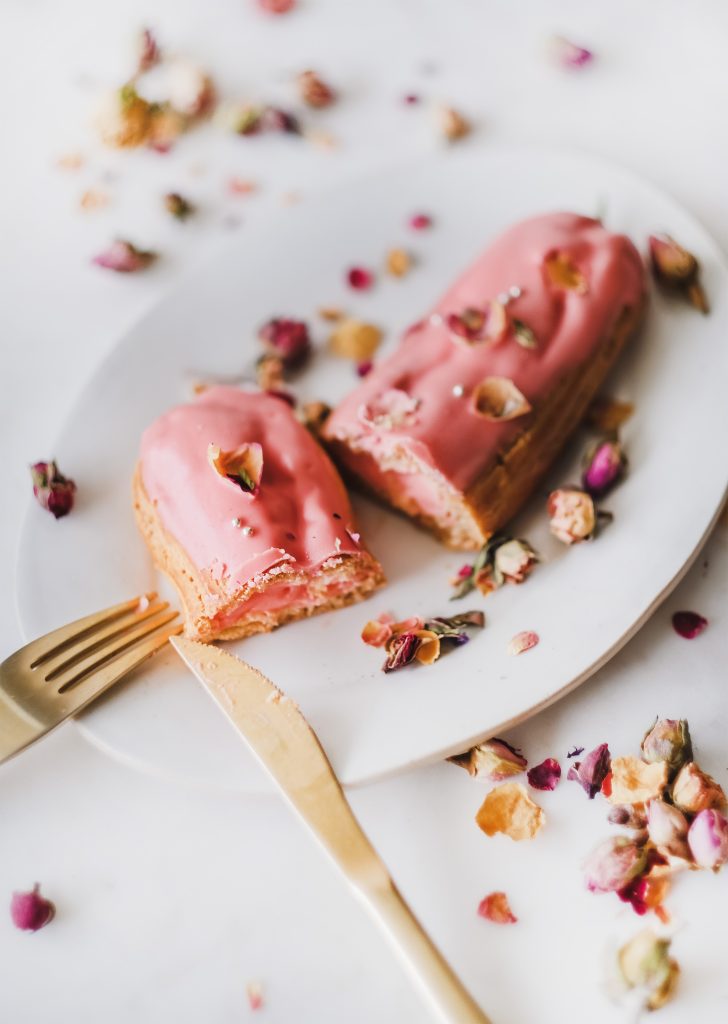 Rose eclair dessert with dried rose petals on white plate